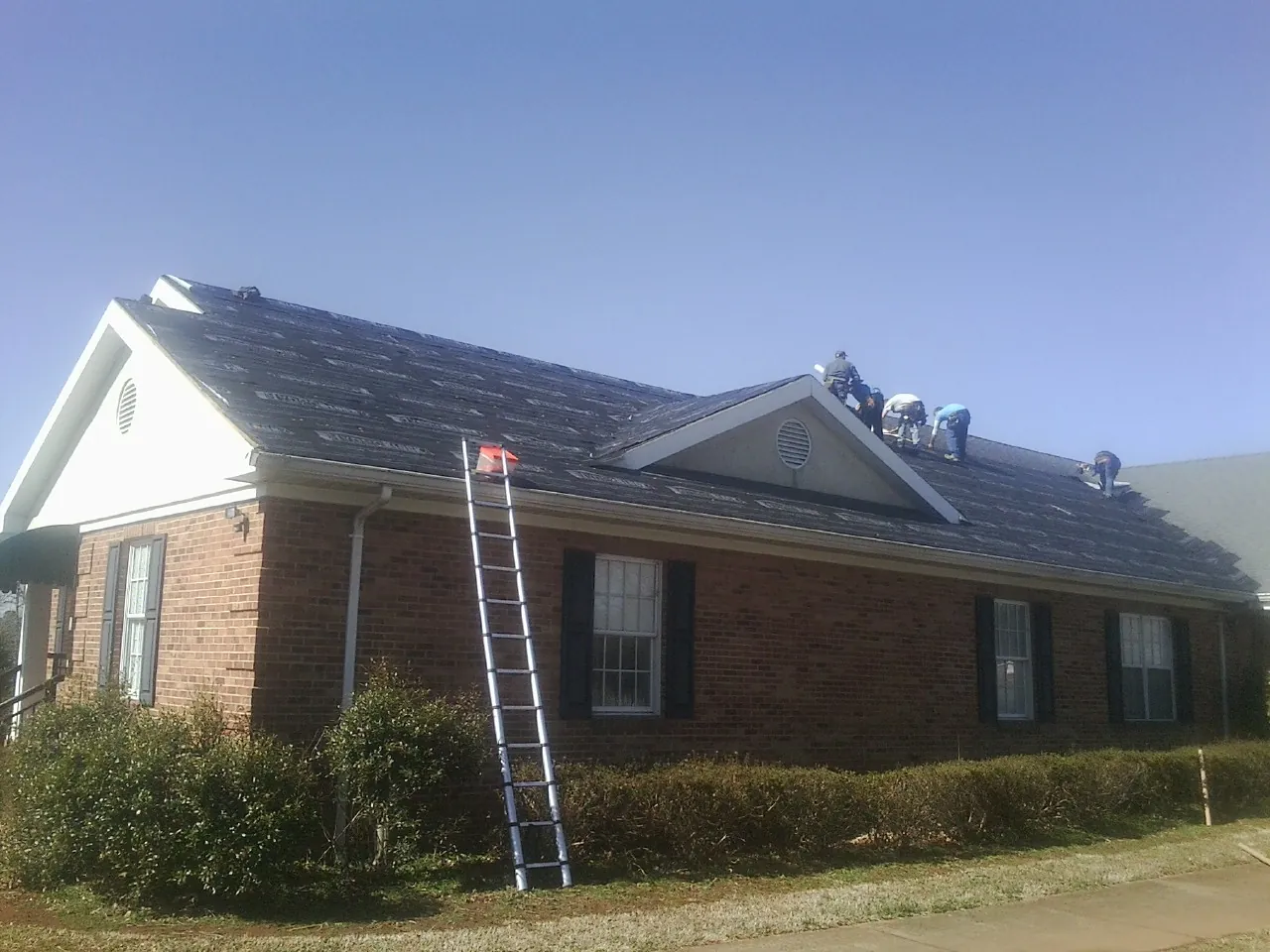 Crew tearing shingles off a brick ranch roof with a ladder set — Emergency Roof Repair work by our crew in New Fairfield