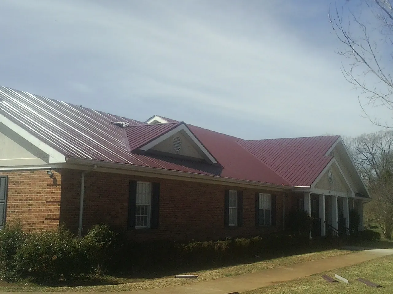 Red metal roof with gabled entries on a long brick building, from a Hail Damage Roof Repair job in New Fairfield