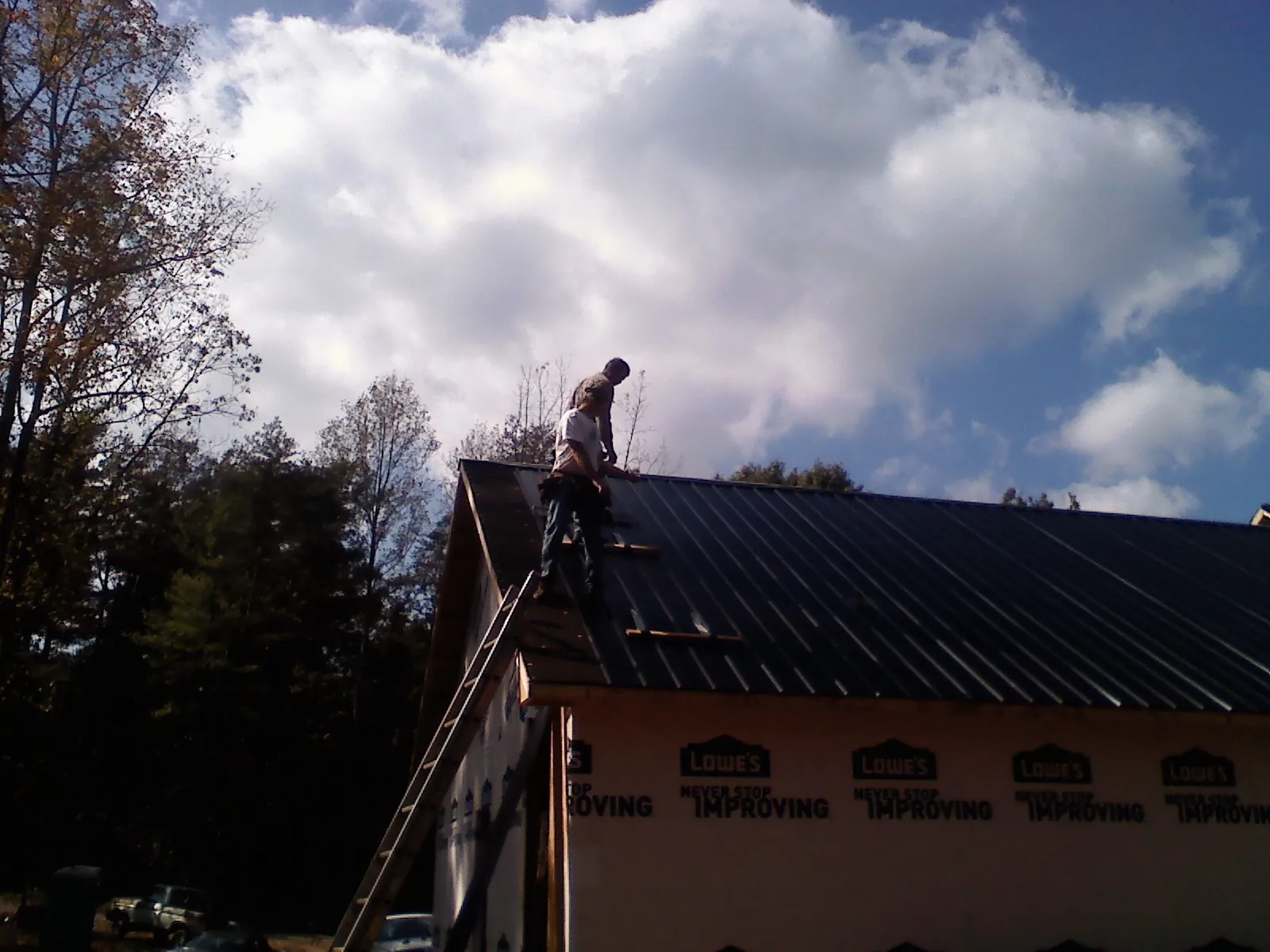 Roofer fastening dark metal panels high against a cloudy sky, from a Roof Inspection job in New Fairfield