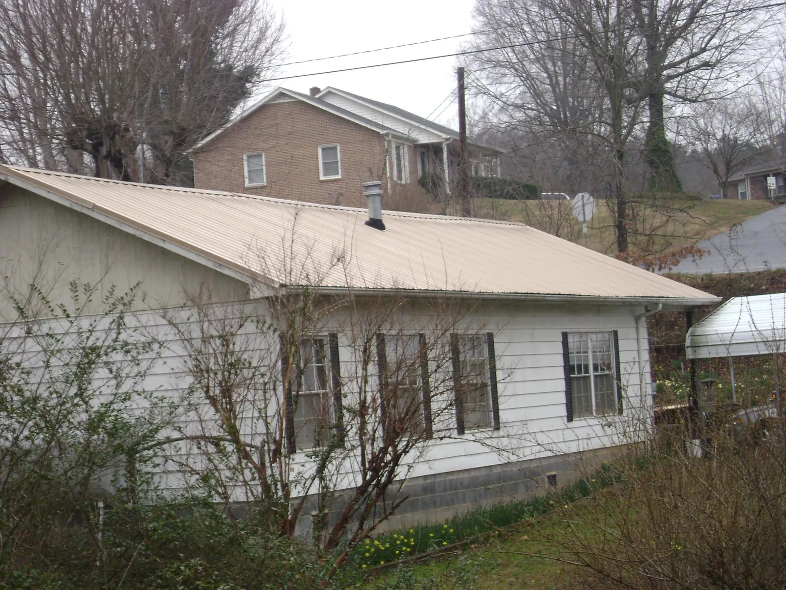 Tan metal roof on a white sided house set into a hillside — Commercial Roofing by Roofing Brothers in New Fairfield